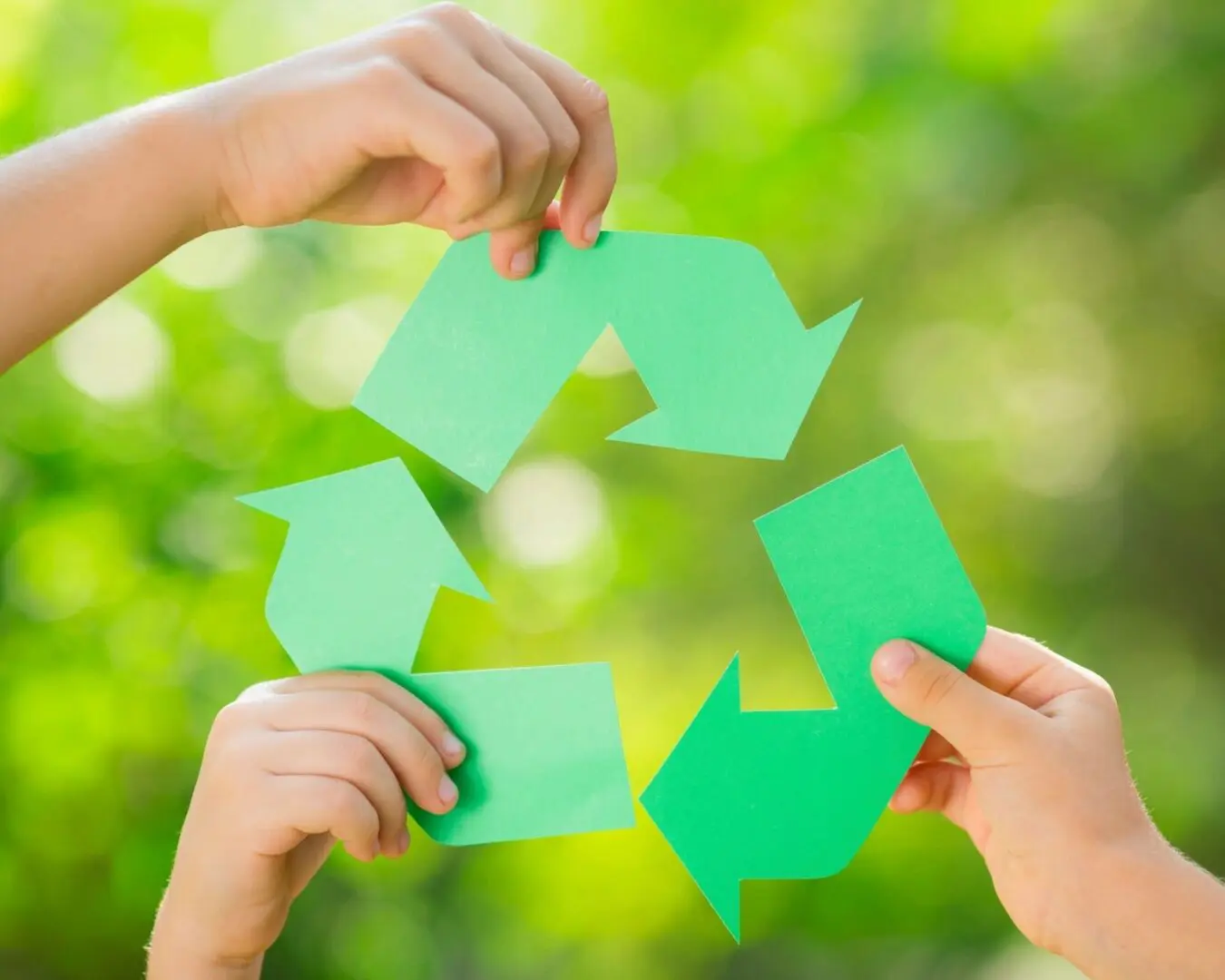 Paper RECYCLE sign in children`s hands against green spring background